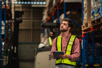 Warehouse workers and manager in reflective vests inspecting inventory, using digital tablet for stock control, logistics, supply chain management, and modern industrial warehouse operations.
