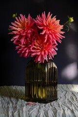 Bouquet of dahlias in green glass vase on dark background with sunlight.Vase of autumn flowers stands on table.Concept: greeting card, autumn holidays. Selective focus. Vertical