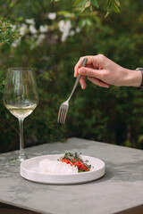 Hand holding fork over fresh burrata with greens and wine