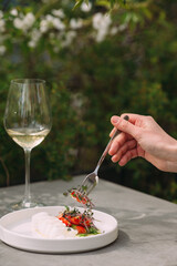 Hand using fork eating gourmet dish with white wine