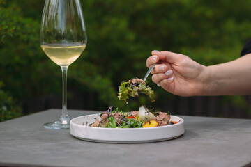Woman eating fresh salad with white wine outdoors