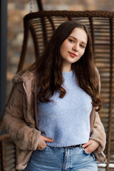 A girl in blue jeans and a warm jacket against the background of a bench.