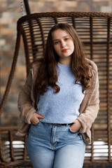 A girl in blue jeans and a warm jacket against the background of a bench.