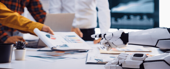 A captivating scene of humans collaborating with a robot in a modern office, showcasing charts and high-tech devices that illustrate innovative teamwork and data analysis.Noogenesis