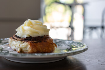 Cinnamon roll with cream frosting on vintage plate. The photo illustrates dessert, indulgence, bakery atmosphere, sweet pleasure, food culture, and culinary concept.
