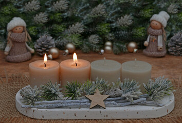 Natürliche Adventsdekoration mit Tannenzweigen, Zapfen und beigen Kerzen, zwei davon brennen zum zweiten Advent.	