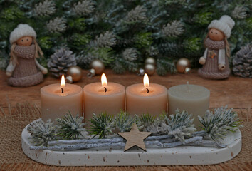 Natürliche Adventsdekoration mit Tannenzweigen, Zapfen und beigen Kerzen, drei davon brennen zum dritten Advent.	