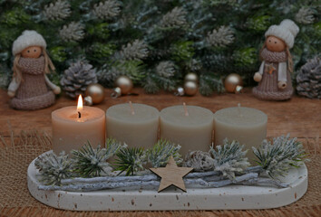 Natürliche Adventsdekoration mit Tannenzweigen, Zapfen und beigen Kerzen, eine davon brennt zum ersten Advent.