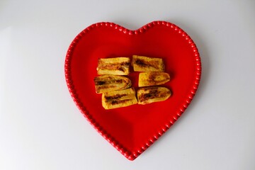 .Slices of ripe fried banana in a red heart seen from above. In the center