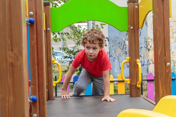 A child in a red shirt captured in dynamic motion while actively climbing on a wooden playground structure