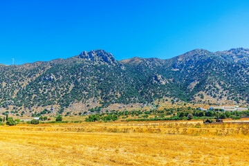 Rocky green mountains on background of dry yellow field with hotel and clear blue summer sky. Greece. Kos.