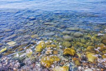 Colorful stones in transparent water on background of clear blue Aegean Sea with small surface waves. Greece.