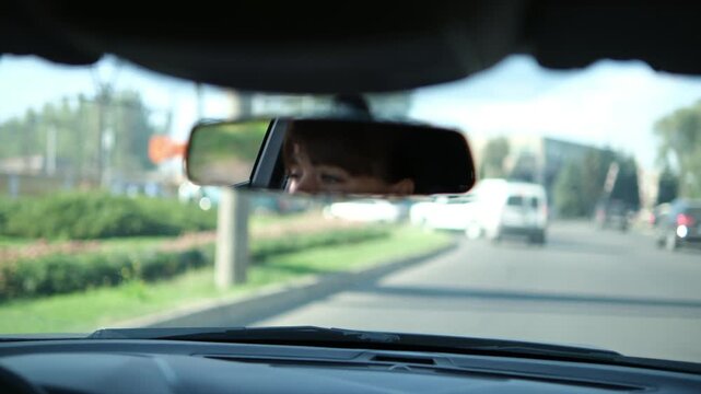 Reflection of a woman's eyes in the rear-view mirror of a car while driving on a city street. The focused driver is commuting during the day, observing the road and traffic