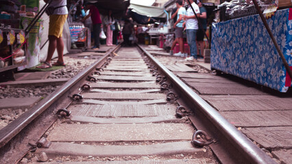 Railway track with people crossing it in a market in Thailand