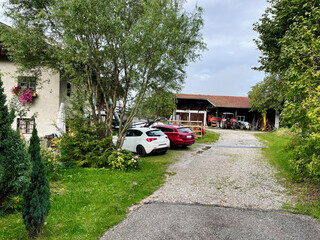 Quiet German farmyard with cars, barn, tractors and lush greenery along a gravel driveway