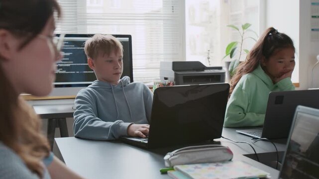 Group of focused middle-school children using laptops during programming lesson in modern school