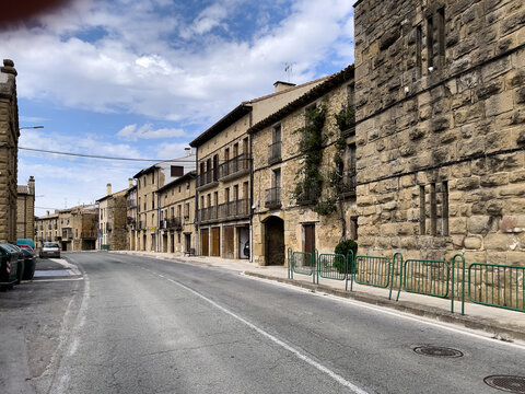 Calle silenciosa con edificios de piedra y balcones de madera, bajo cielo parcialmente nublado en un entorno hist&oacute;rico.