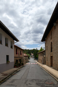 Calle estrecha de pueblo con casas de madera y piedra, tejados inclinados y flores en las ventanas bajo cielo gris.