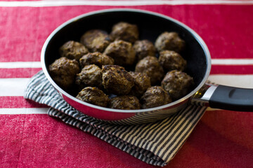 Homemade Swedish meatballs served in a frying pan on a red tablecloth, symbolizing traditional Nordic comfort food. 
