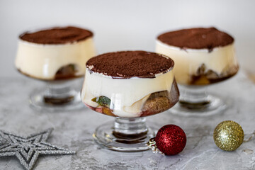 Individual tiramisu servings in glass cups topped with cocoa powder, styled with Christmas ornaments on a light background. Perfect for holiday dessert menus and festive celebrations.