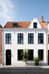 Newly renovated white town house with modern windows and traditional roof in a charming European street under a clear blue sky