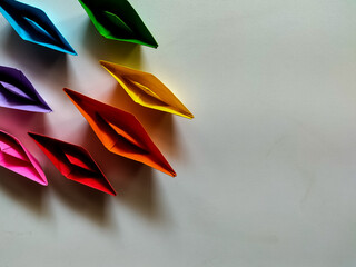 Colorful paper boats made from vibrant origami paper are arranged on a smooth, light-colored...