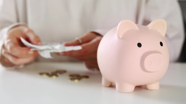 A woman looks through bills and checks and puts money and coins into a piggy bank that she has saved. Savings concept and income management deposit