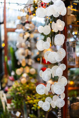 A close-up of a decorative wind chime or garland made of translucent capiz shells. The shell discs are round, with a spiral pattern, and christmas lights are in the blurred background.