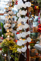 A close-up of a decorative wind chime or garland made of translucent capiz shells. The shell discs are round, with a spiral pattern, and christmas lights are in the blurred background.