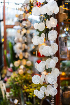 A close-up of a decorative wind chime or garland made of translucent capiz shells. The shell discs are round, with a spiral pattern, and christmas lights are in the blurred background.
