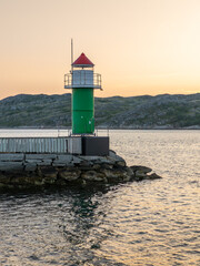 24 juli 2025, Bodø, Norway. Lighthouse on the pier in Bodo, Bodø, a port city in Norway. Beautiful warm light during sunset, a golden sky, low mountains in the background. Water in the fjord in the fo