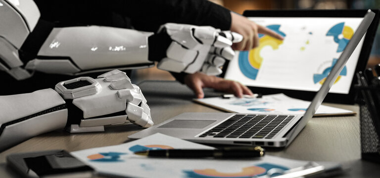 A futuristic workspace showcasing a human collaborating with a robotic arm, analyzing digital designs and creative concepts on a laptop, emphasizing innovation and teamwork.Noogenesis