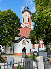 Church St. Sebastian Puch in Furstenfeldbruck, Germany with red roof clock tower, surrounded by trees and graveyard, historic architecture