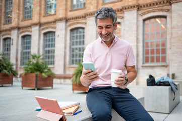 Smiling man using smartphone taking coffee break outdoors
