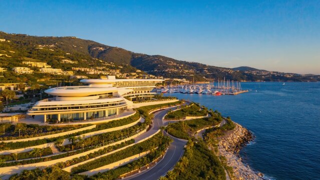 Luxury seaside resort with modern architecture along a scenic coastline, surrounded by green hills and yacht marina, illuminated by warm golden sunlight during a calm summer sunset, evoking relaxation