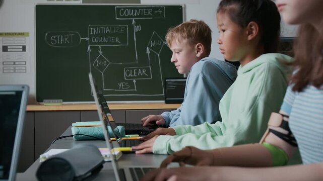 Group of middle-school students struggling with their assignment, working on laptops during IT class in school