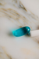 close up of blue liquid gel and white pill capsule on white marble bathroom countertop