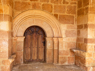 The ancient Romanesque and Mozarabic portal with a rustic wooden door at the Church of Saint Pelagius in Pisón de Ojeda, Spain