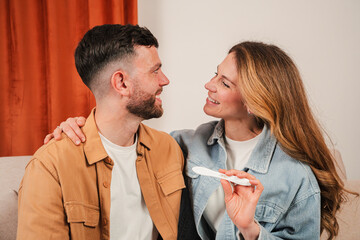 Happy couple cherishing a moment of joy as they hold a positive pregnancy test in a cozy living space filled with warmth and affection, expressing their love and excitement for the future together.