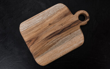 Rustic wooden cutting board with hanging hole on black textured background, ideal for cooking, gastronomy and culinary presentations.