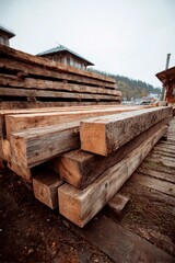 Stacks of wooden logs rest on a wooden platform at a lumber yard. The setting is misty and tranquil, surrounded by trees and a calm atmosphere