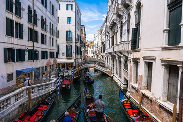 Fototapeta premium Classic Venetian canal view with gondolas gliding through narrow waterways lined with historic buildings under a blue, partly cloudy sky.