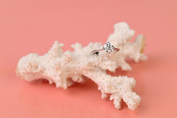 An engagement diamond ring is on top of a coral