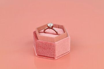 A engagement diamond ring is in a pink velvet jewelry box
