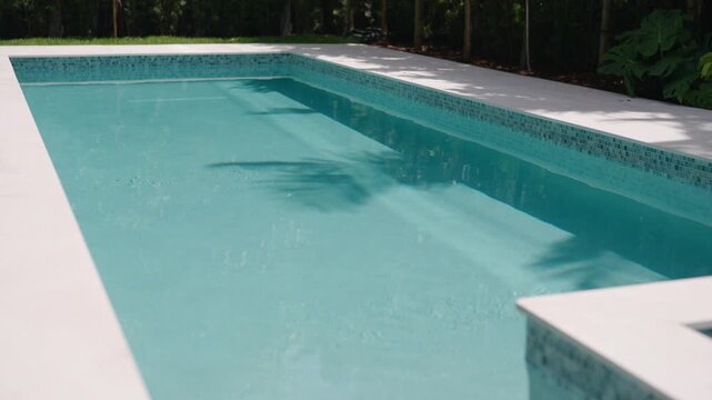 Modern swimming pool with clear water and light deck around it. Smaller square section that looks like hot tub. Pool has clean tile border and surrounded by tall green trees