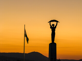 Obraz premium The Hungarian flag and Liberty statue's shape on the orange sunset lights in Budapest city. Capital of Hungary