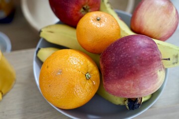 A bowl of apples, oranges, bananas, and pomegranates on a table