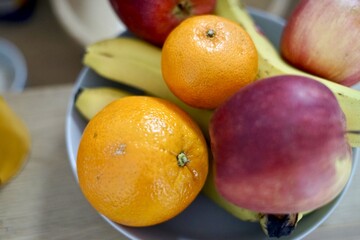 A bowl of oranges, bananas, apples, and pomegranates on a table