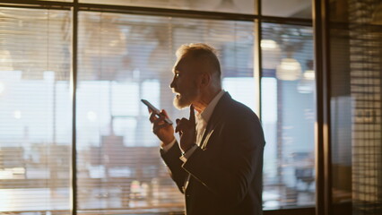 Businessman recording voice message on smartphone walking hall sunlight closeup