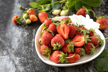 Fresh summer strawberries in white bowl on dark rustic surface